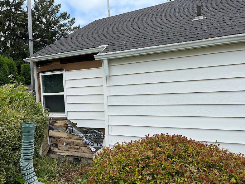 Damaged house siding and window with broken lower wall and debris near bushes