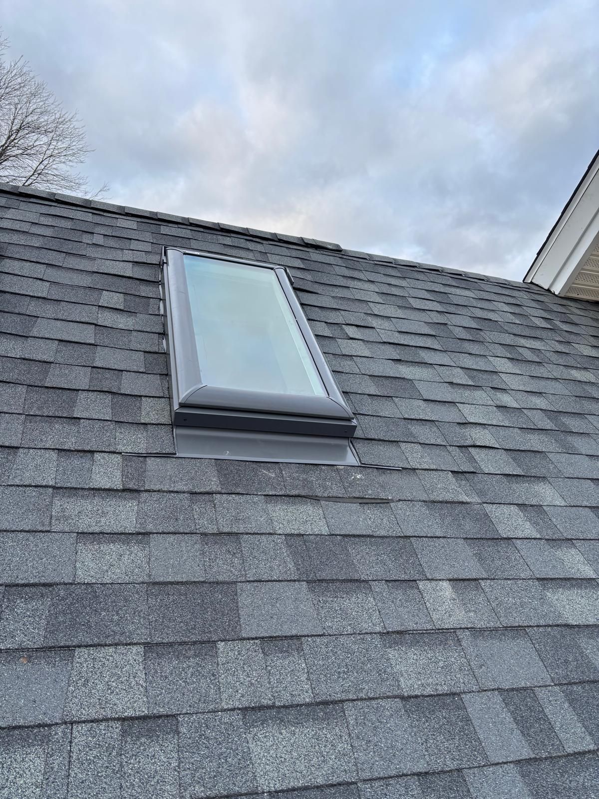 Roof with gray shingles and a skylight under a cloudy sky