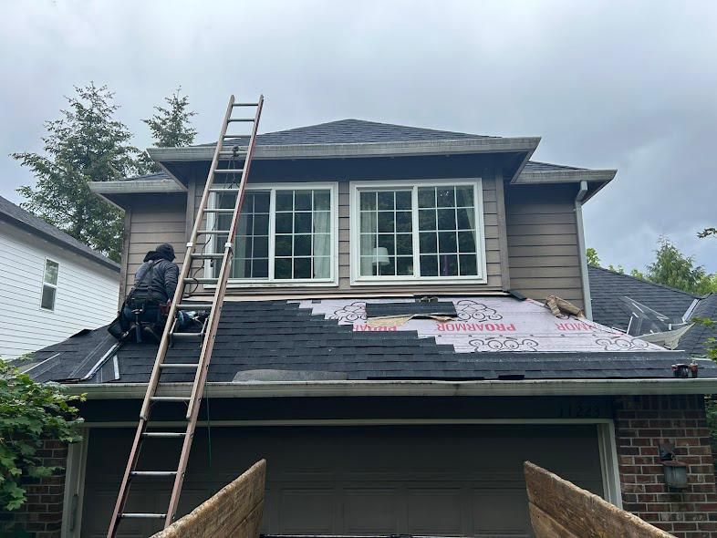 Workers installing roofing on a house with a ladder and underlayment exposed