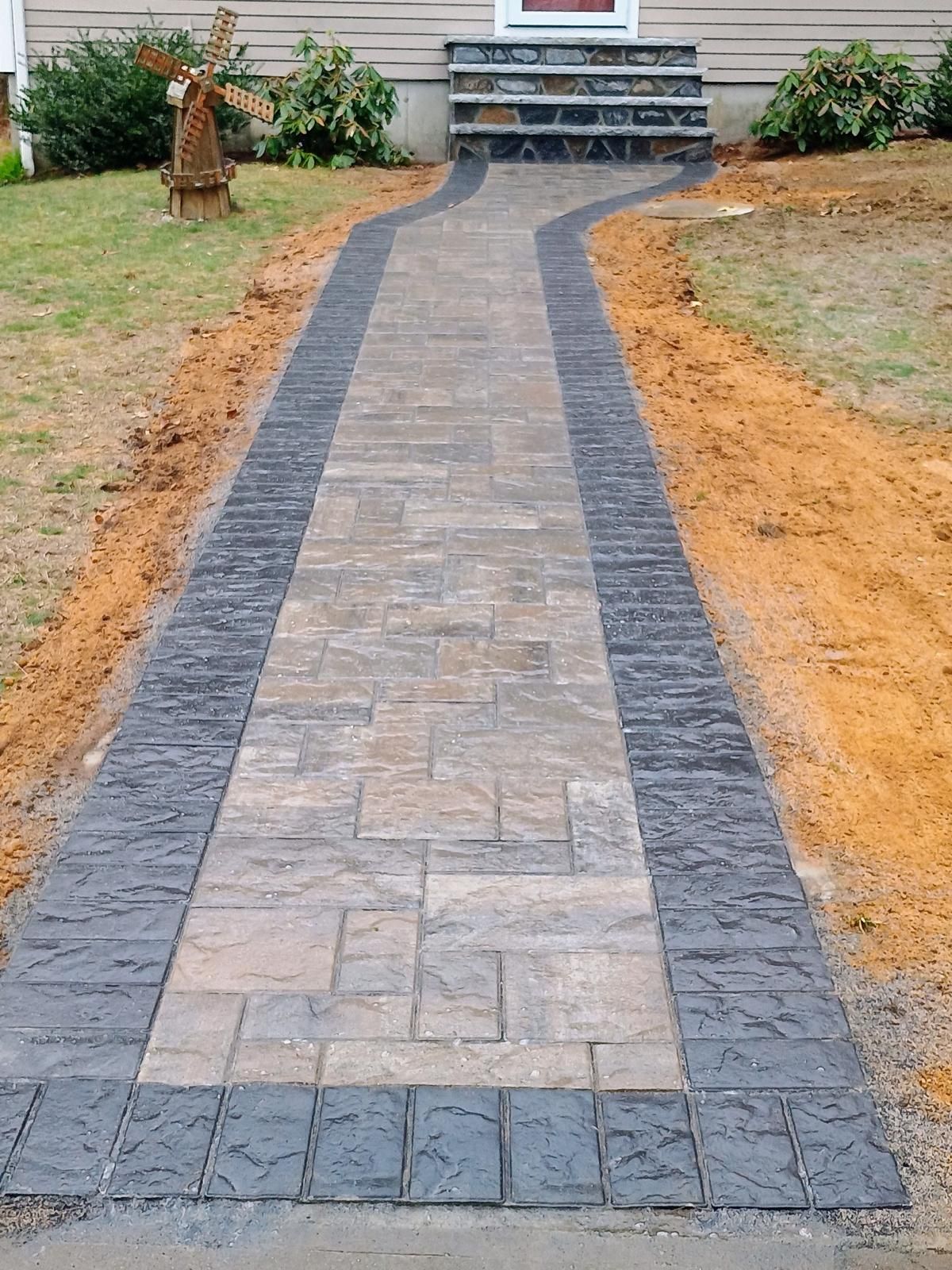 Stone walkway with dark border leading to a house entrance through a landscaped yard