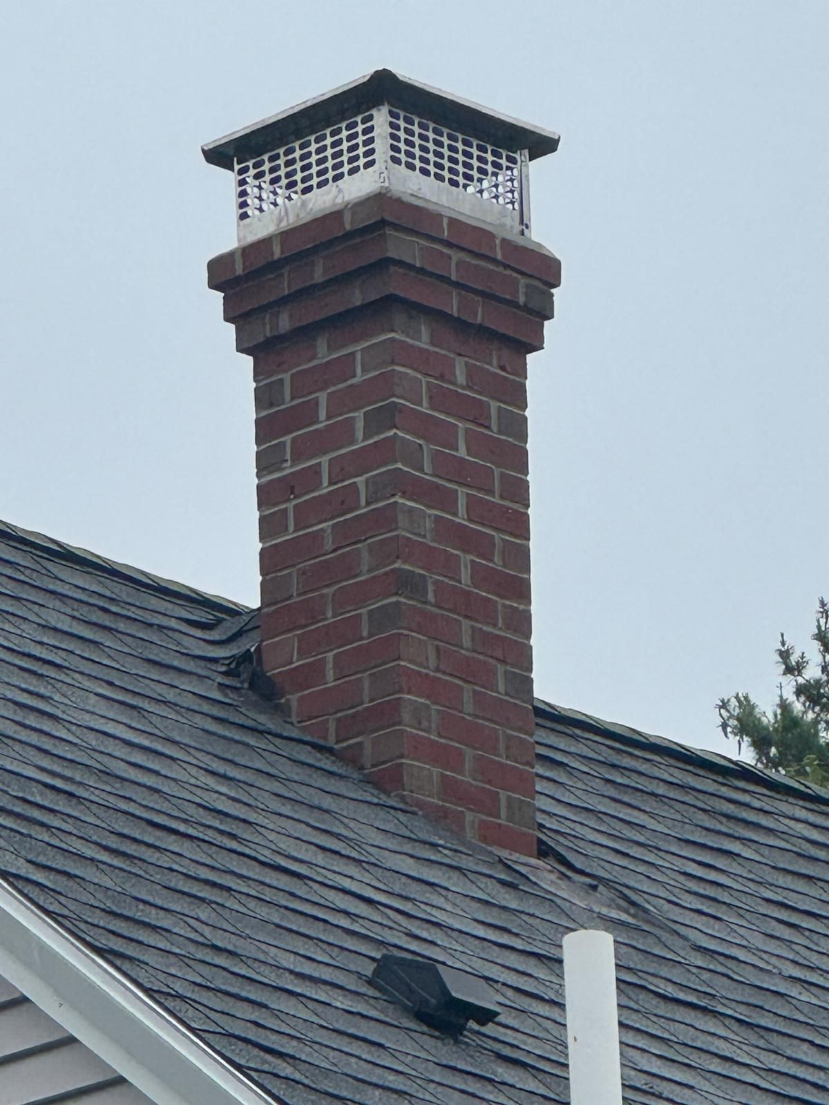 Brick chimney with a white cap on a gray shingled roof against an overcast sky