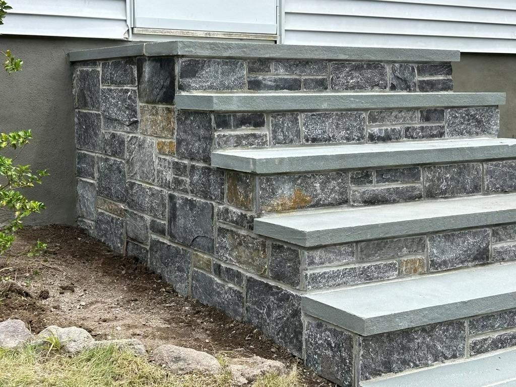 Stone retaining wall with concrete steps leading up to a patio area