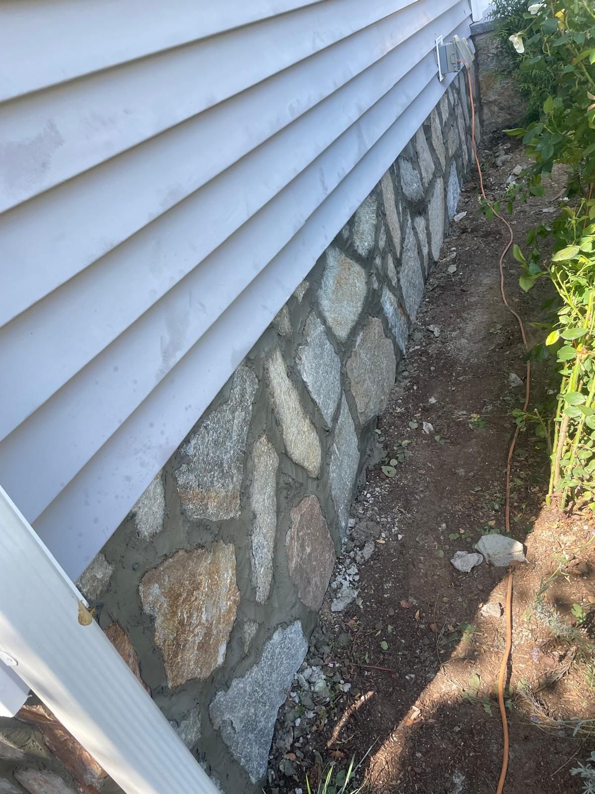 House siding with stone foundation and narrow dirt strip along the side yard