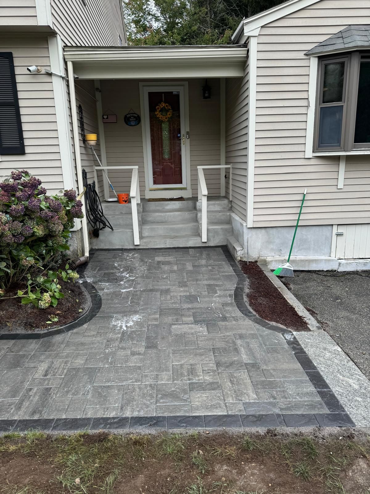 Front porch with new gray paver walkway, white railings, and a red front door.