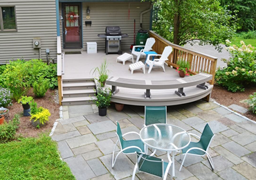 Backyard patio with white deck chairs, teal chairs around a glass table, and a landscaped stone patio.