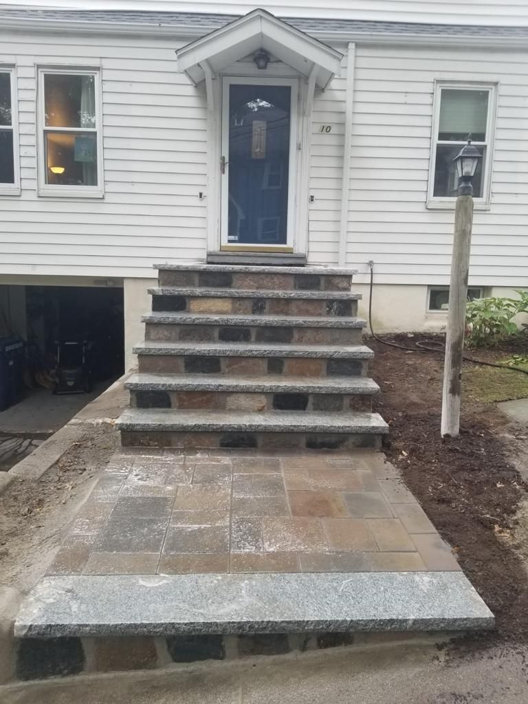 Front entrance with blue door, stone steps, and a paved landing on a white house