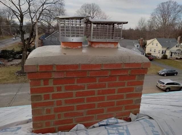 Brick chimney with two metal caps on a rooftop overlooking a residential street in winter
