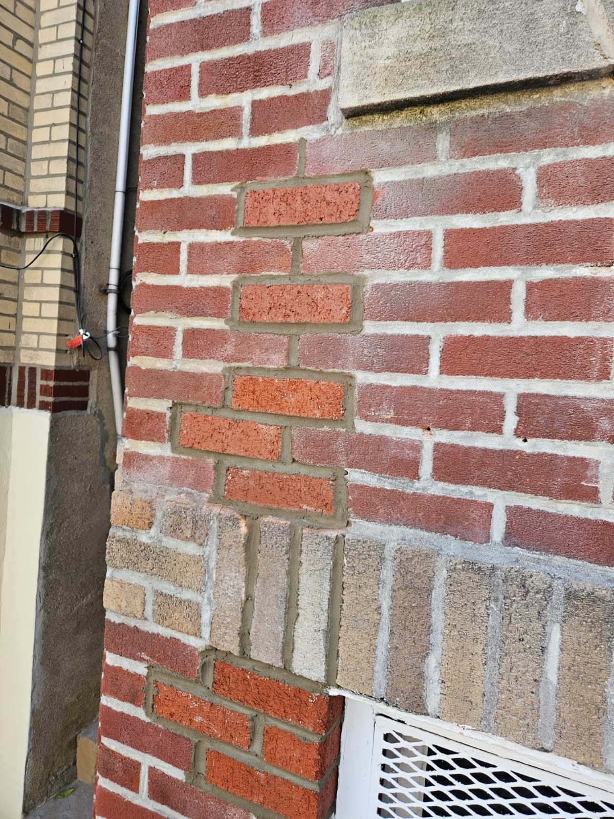 Brick wall with varied red, tan, and gray bricks next to a vent and doorway edge