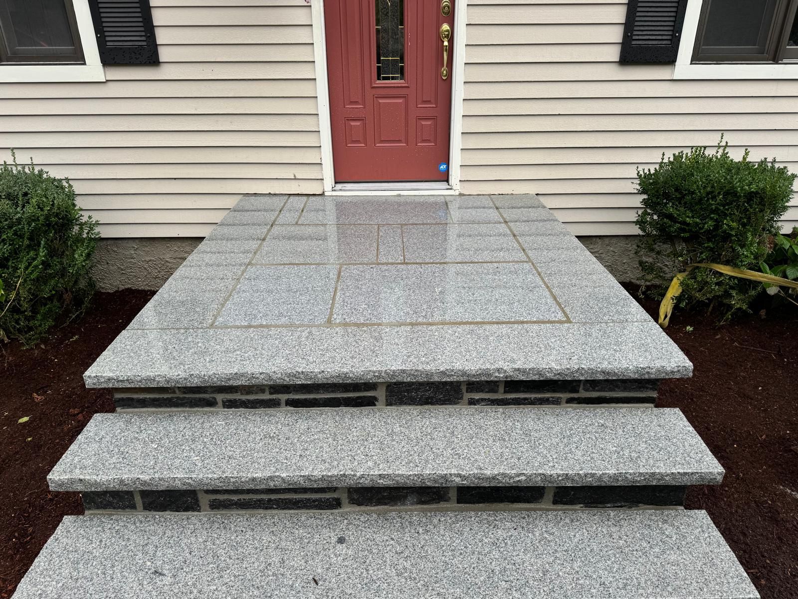 Front steps and a granite landing leading to a red front door