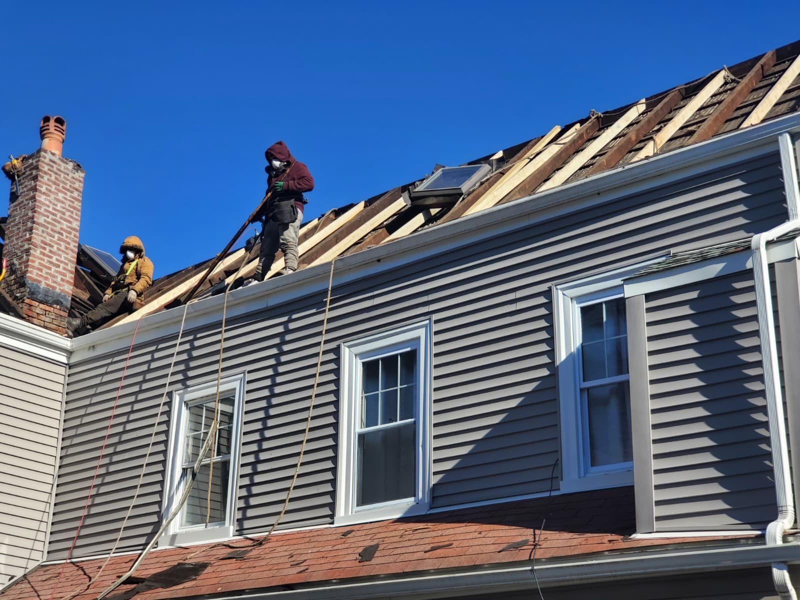 Workers repairing a house roof with ladders on a sunny day