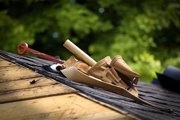Wooden hand planes and a red screwdriver on a weathered roof, with blurred greenery in the background