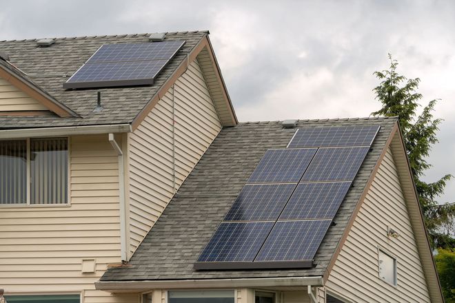 Two house roofs with solar panels under a cloudy sky