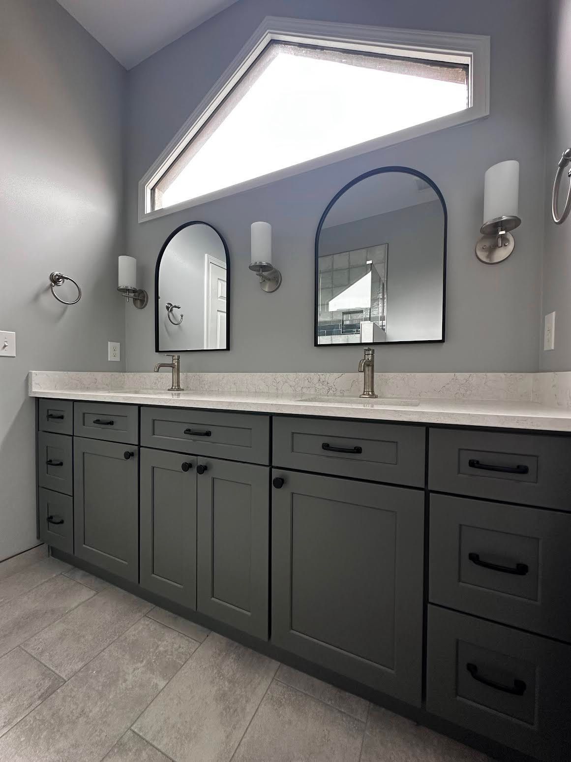 A bathroom with two sinks , two mirrors and a window.
