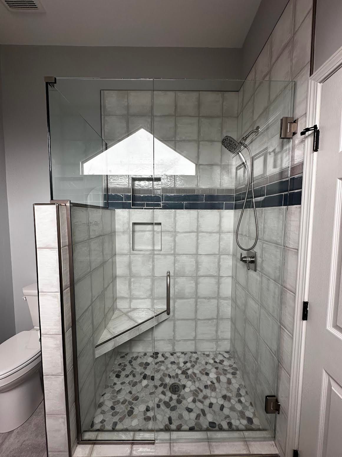 A bathroom with a walk in shower with a glass door and a toilet.