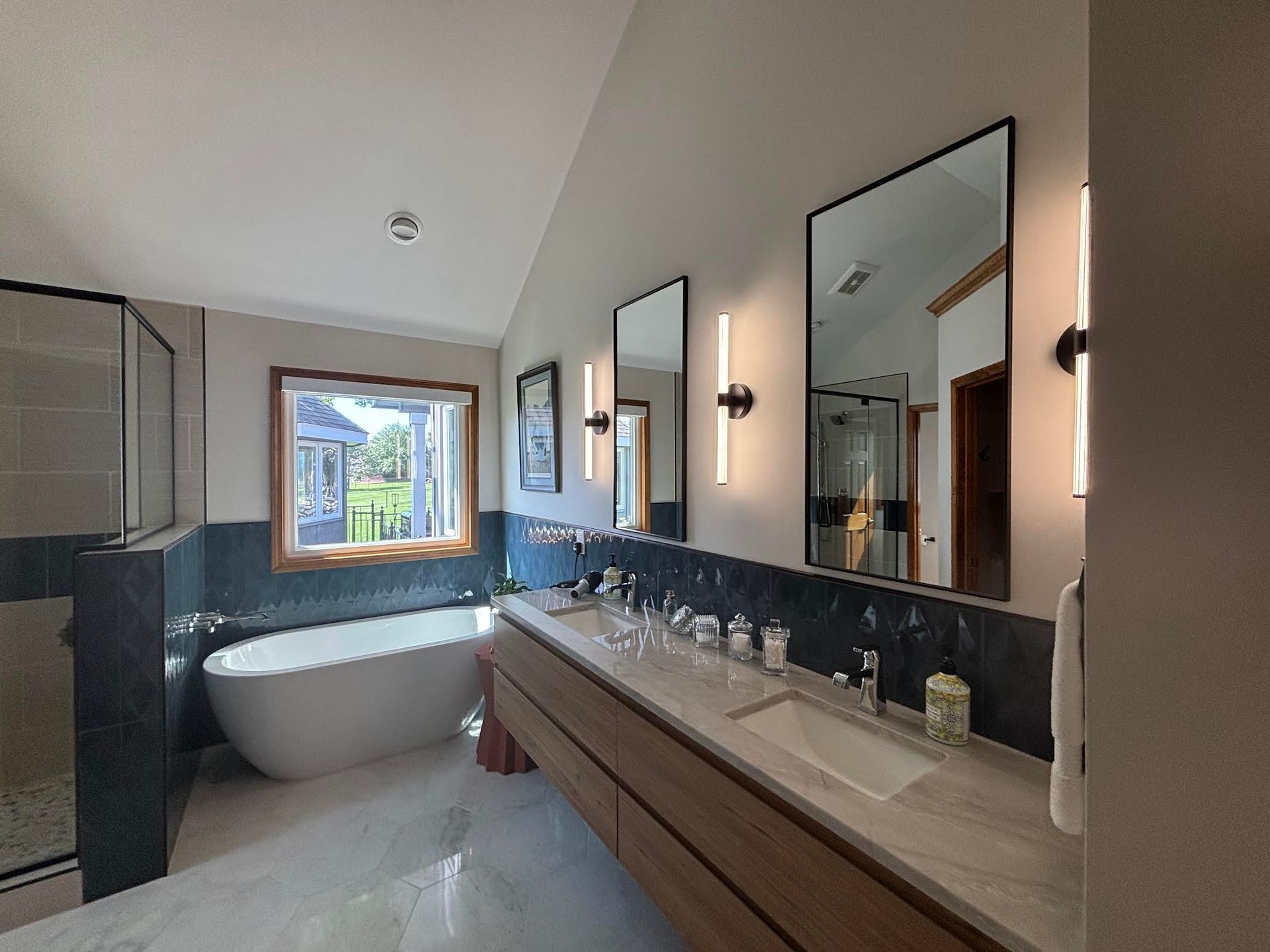 A bathroom with a tub, sinks, mirrors and a window.