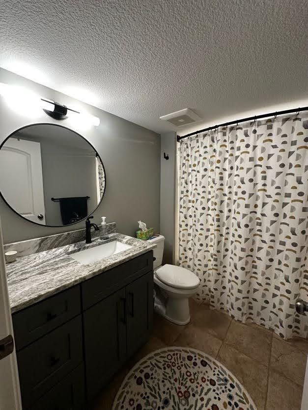 A bathroom with a toilet, sink, mirror and shower curtain.