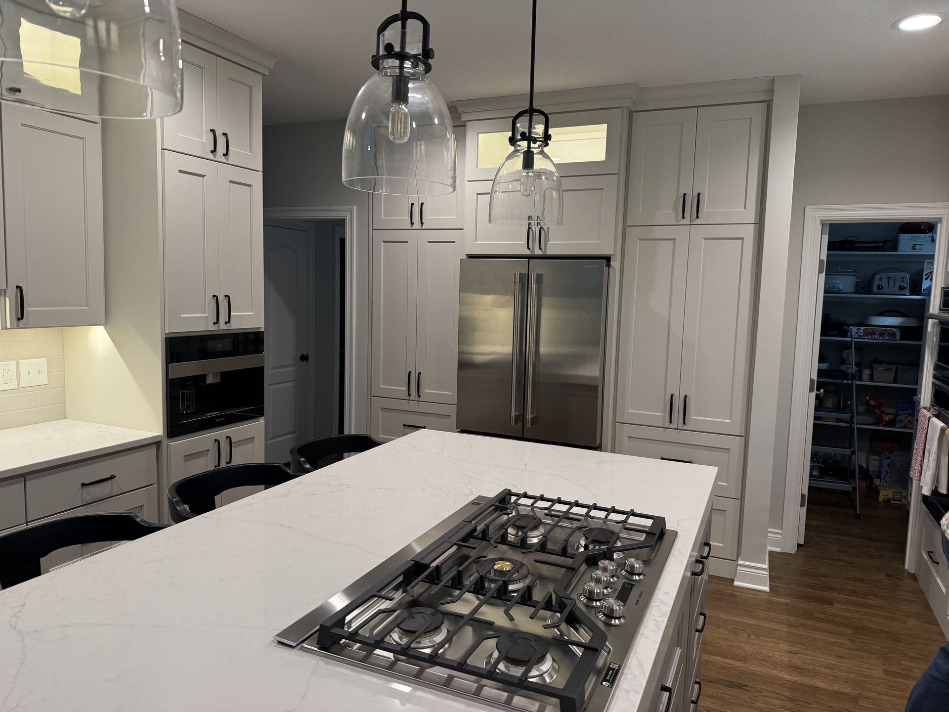 A kitchen with white cabinets, a stove top oven, a refrigerator, and a large island.