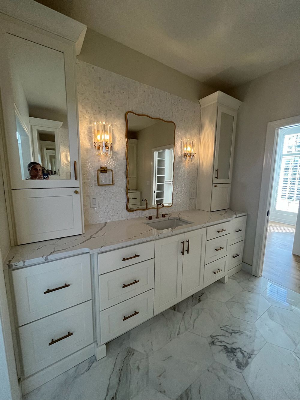 Bright white bathroom vanity with marble floor, mirrored cabinets, sconces, and glass shower door