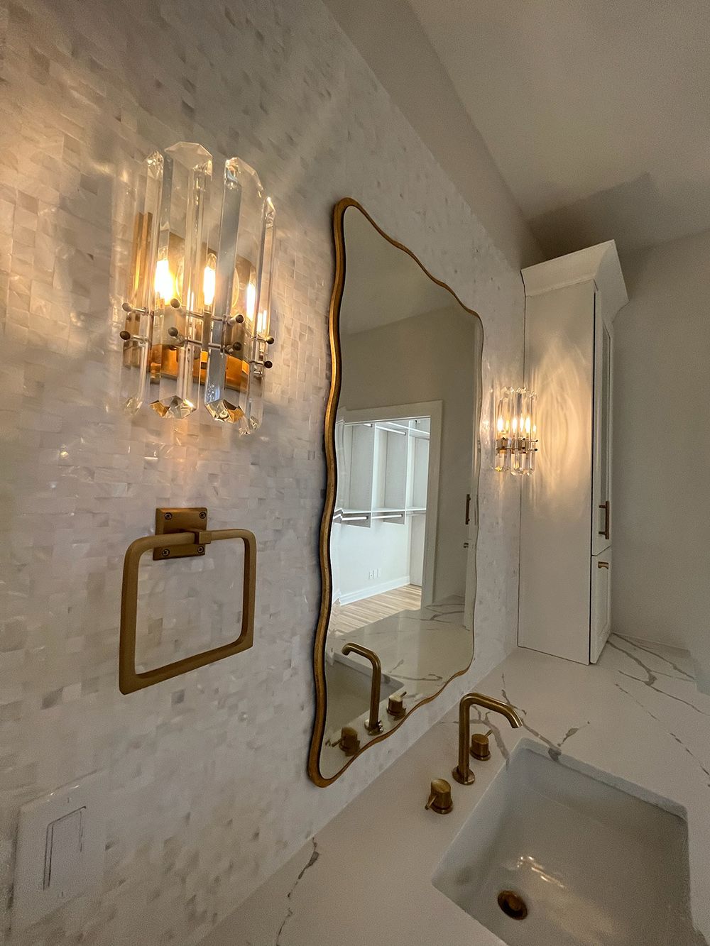 Small white bathroom with a gold-framed mirror, wall sconces, and a vanity sink.