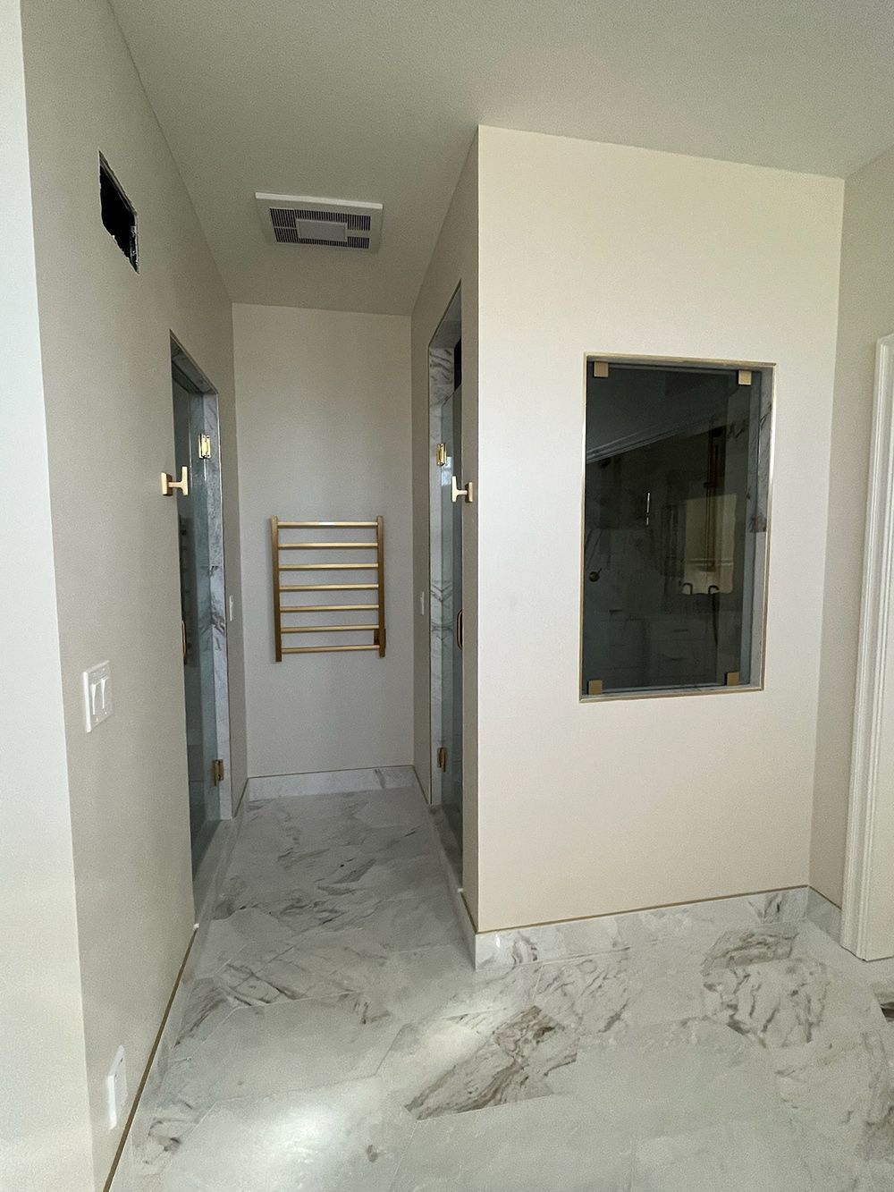 Narrow unfinished hallway with marble floor, beige walls, and a towel rack at the far end.