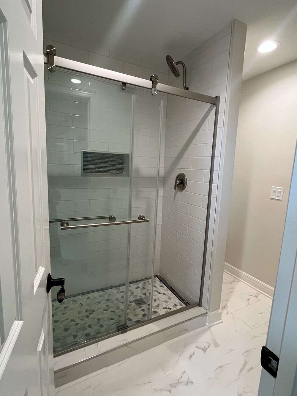 Modern glass shower enclosure with chrome fixtures and tiled floor in a bright bathroom