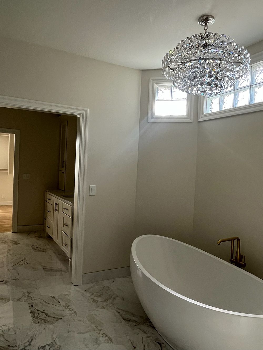 Elegant bathroom with a freestanding tub, crystal chandelier, and marble-look floor tiles