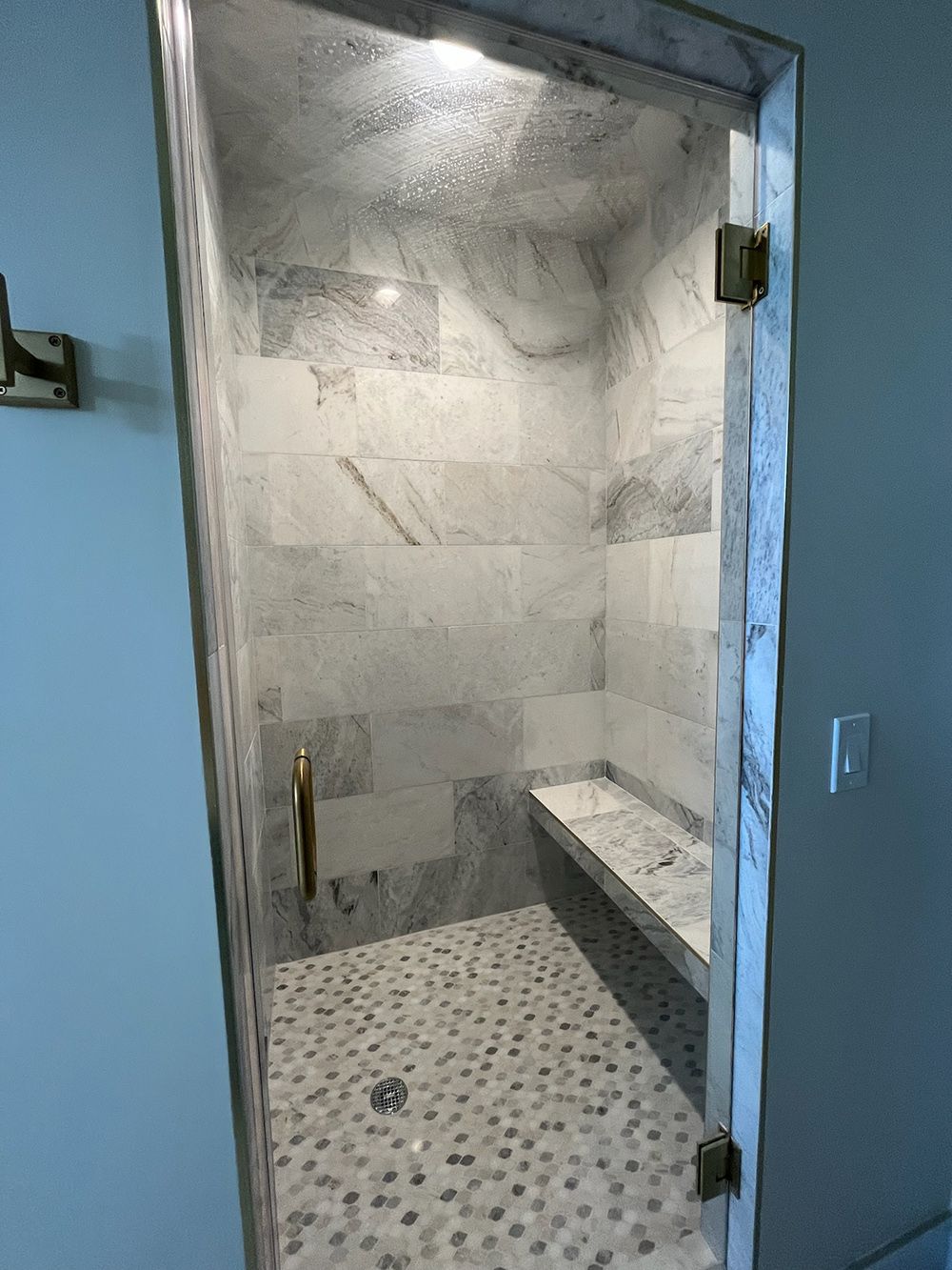 Modern tiled shower with pebble floor, bench, and glass door in a bathroom