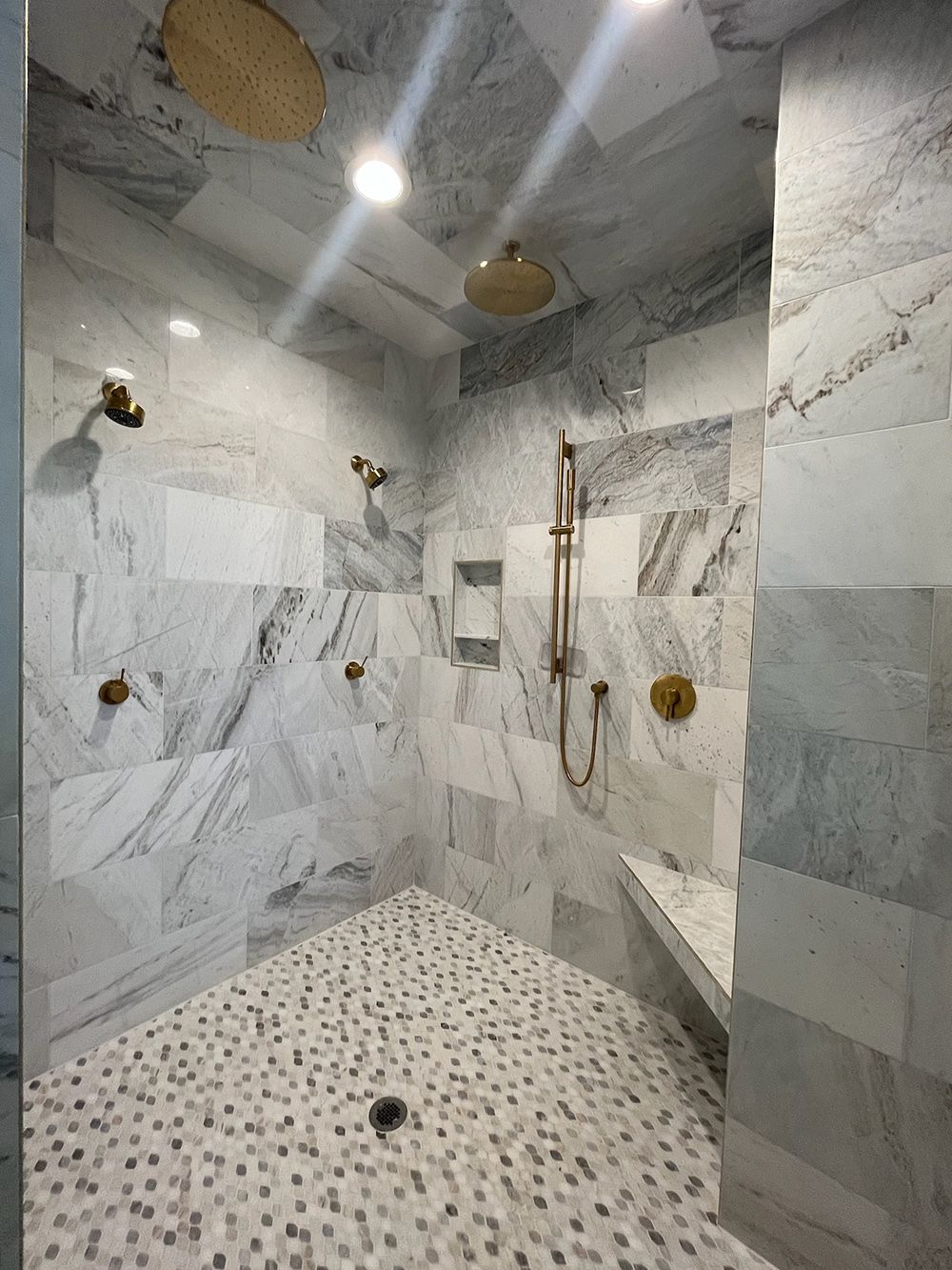 Modern marble-tiled walk-in shower with multiple showerheads and a pebble floor