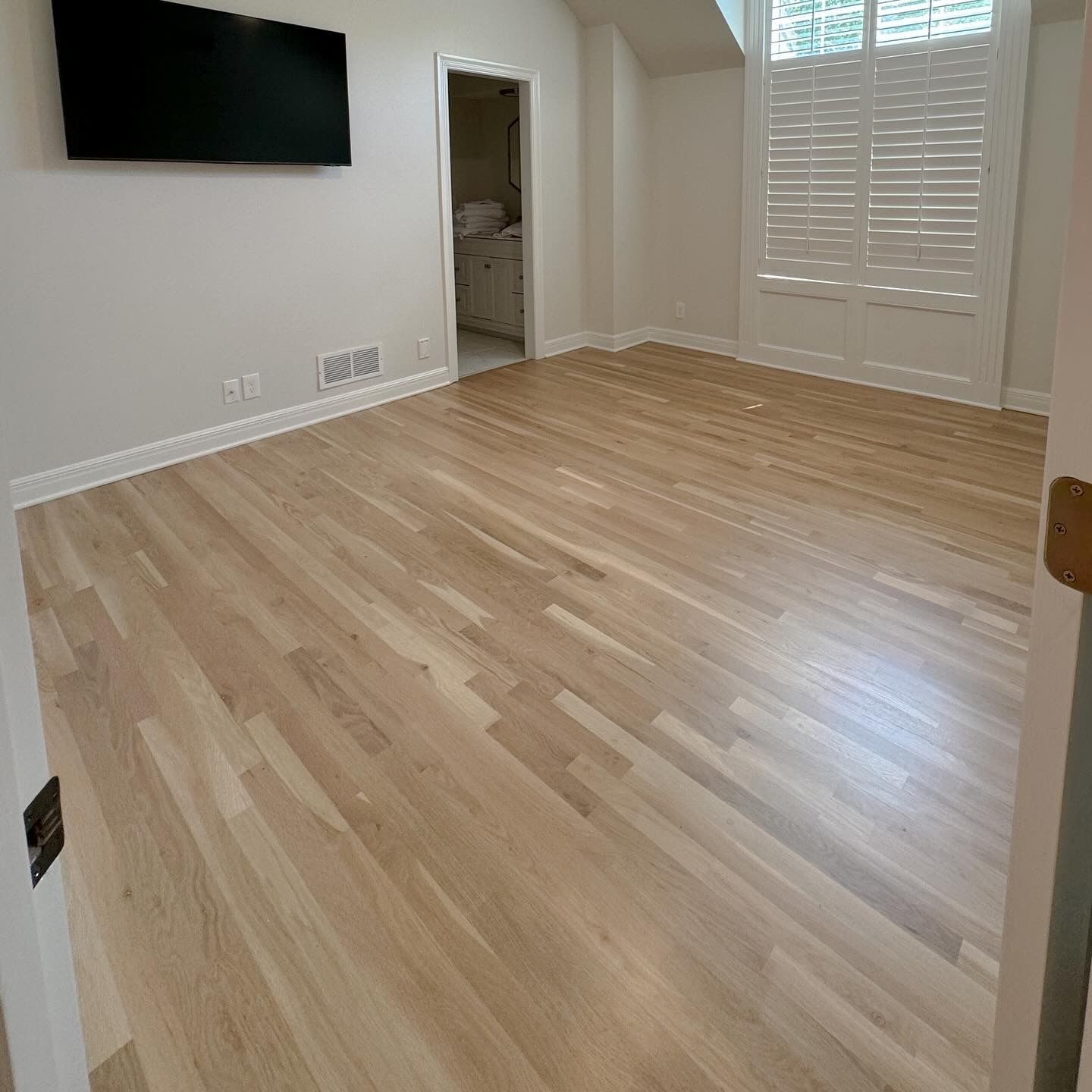 A bedroom with hardwood floors and a flat screen tv on the wall.