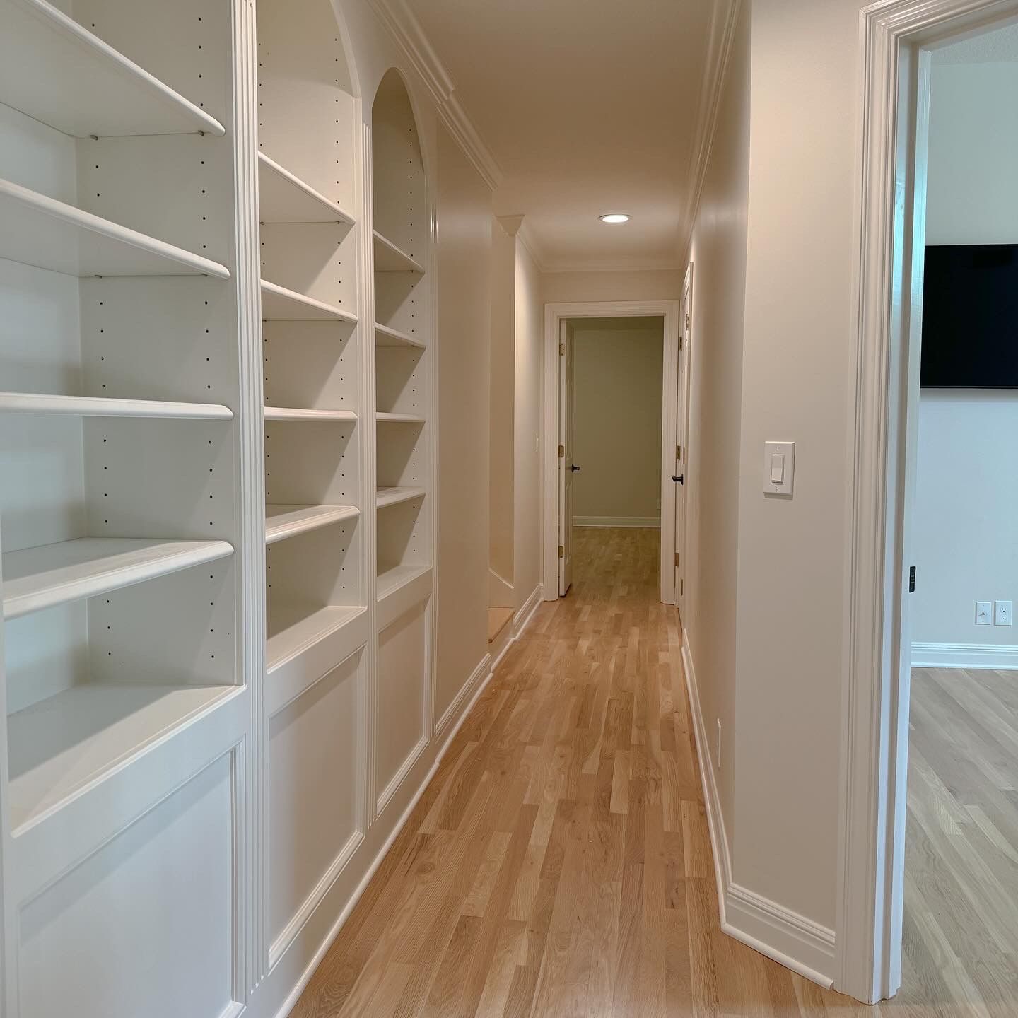A hallway with white shelves and hardwood floors