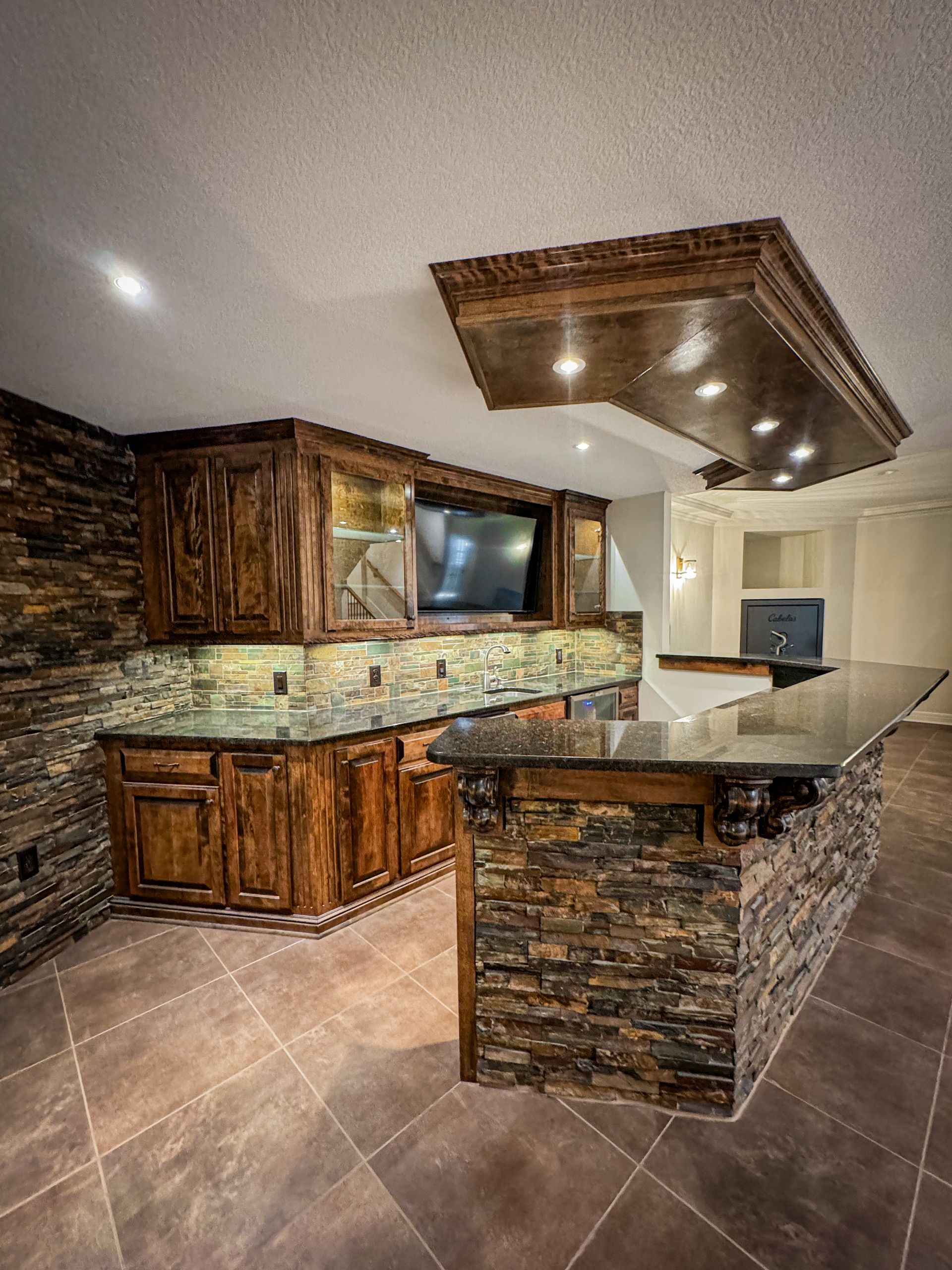 A kitchen with a stone wall, granite counter tops, and wooden cabinets.