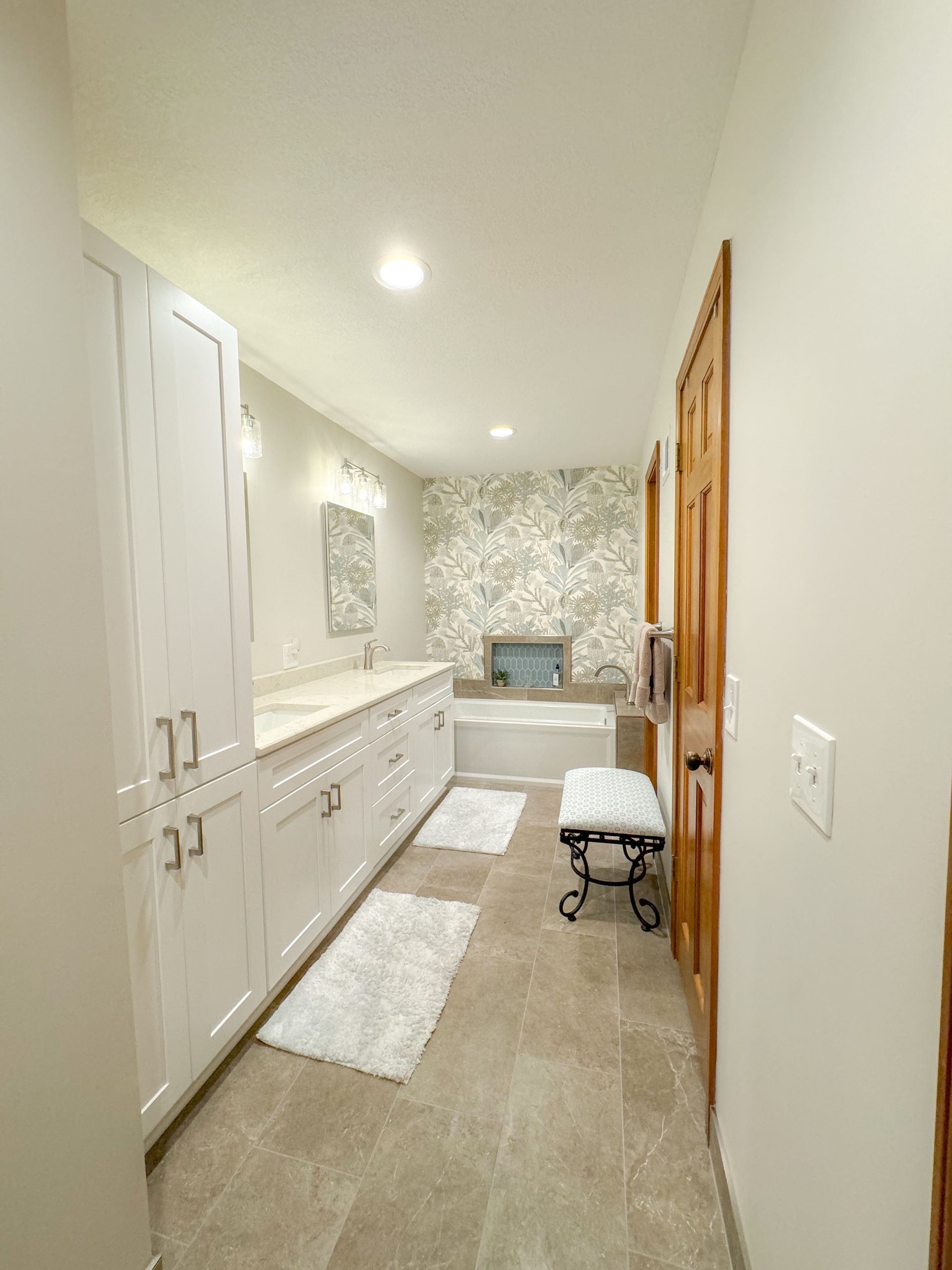 A bathroom with white cabinets, a tub, a mirror, and a bench.