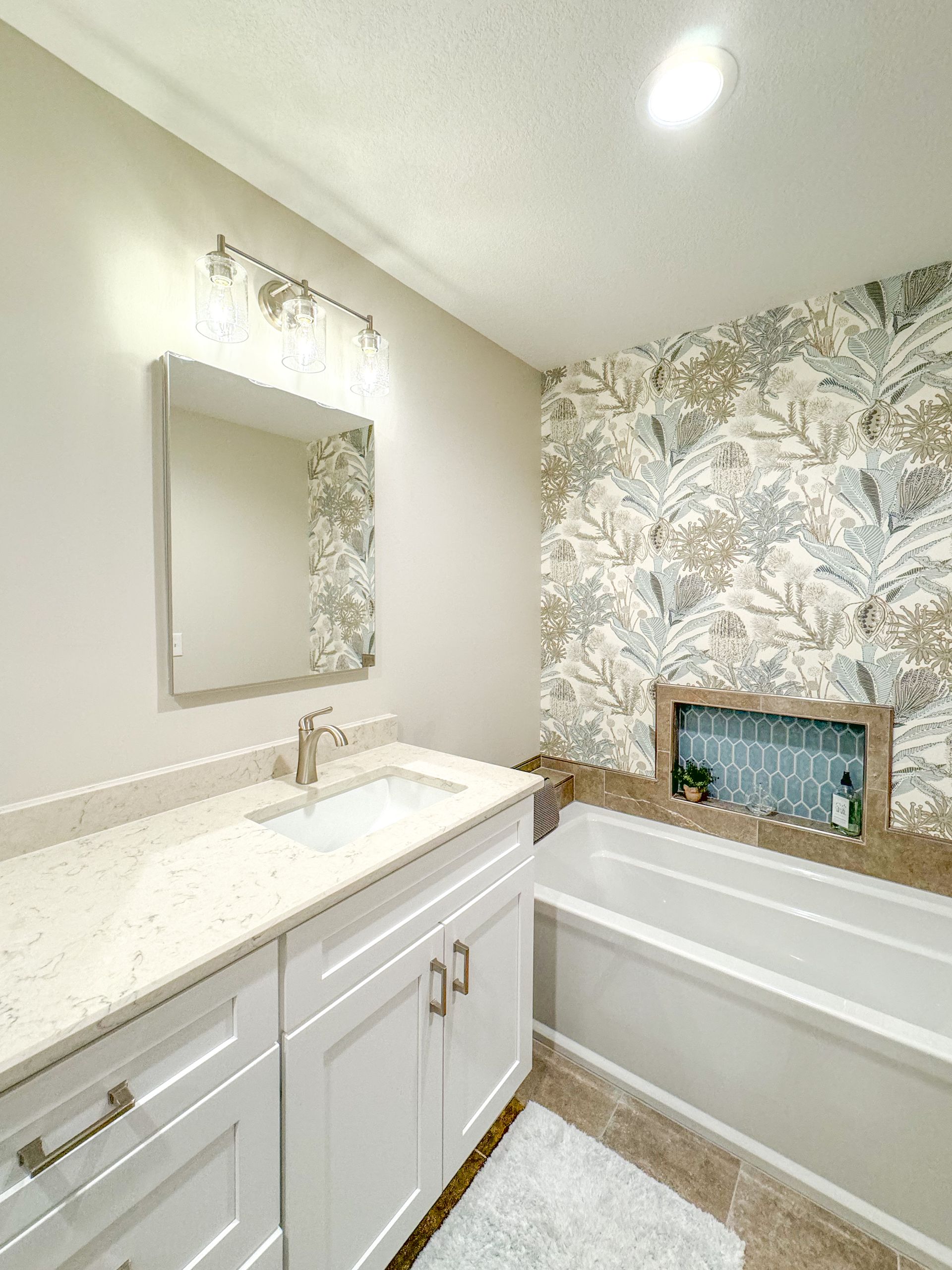 A bathroom with a sink, bathtub, mirror, and marble wall.