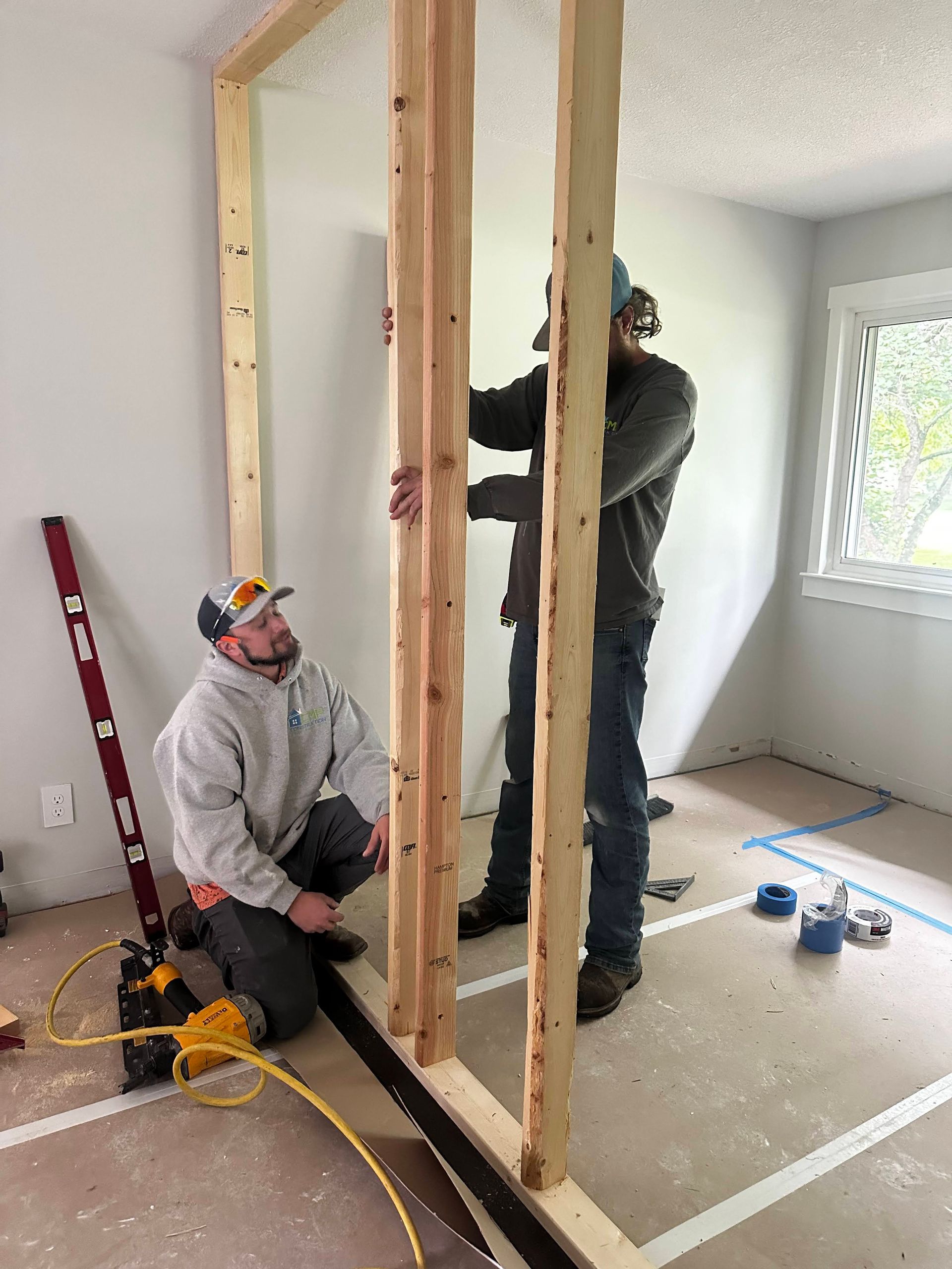 Two men are working on a wooden wall in a room.