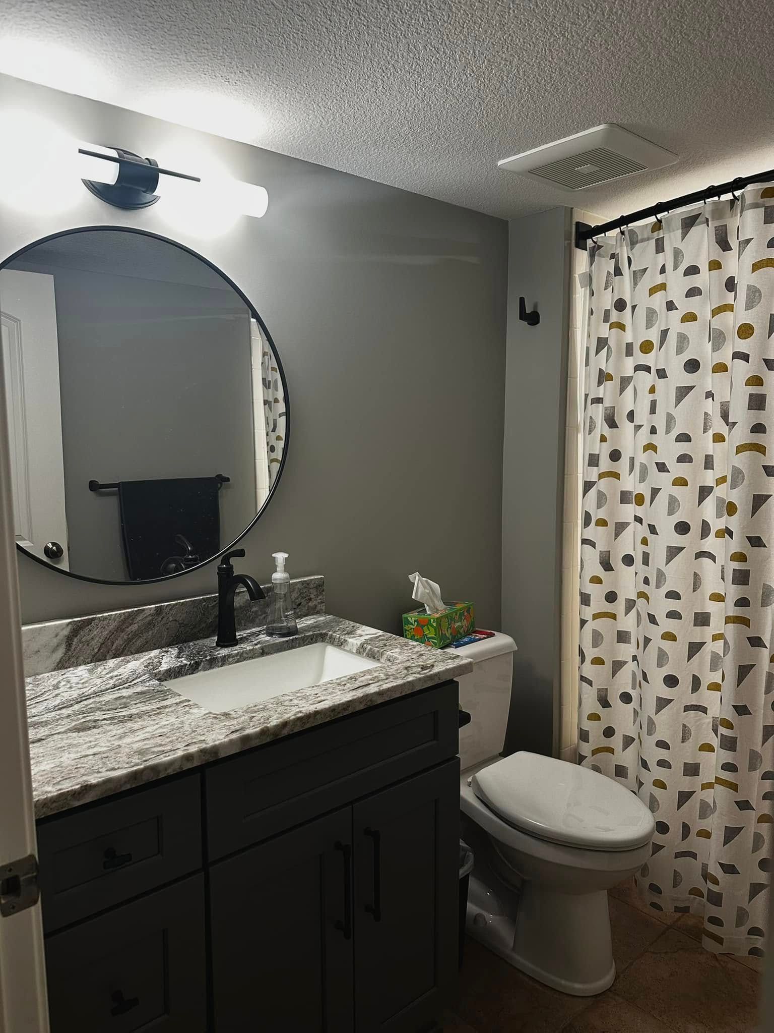 A bathroom with a toilet , sink , mirror and shower curtain.