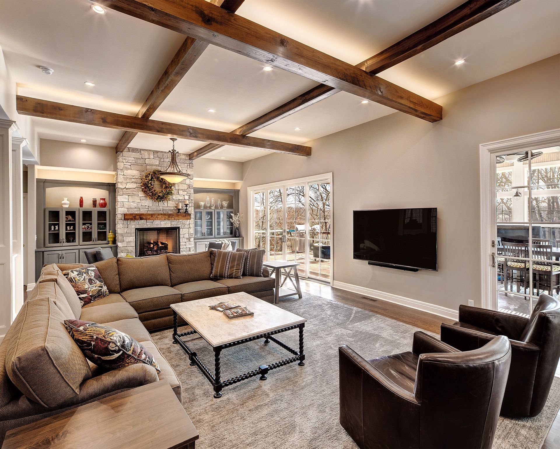 Living room with sectional sofa, fireplace, and TV, with wooden beams and large windows.