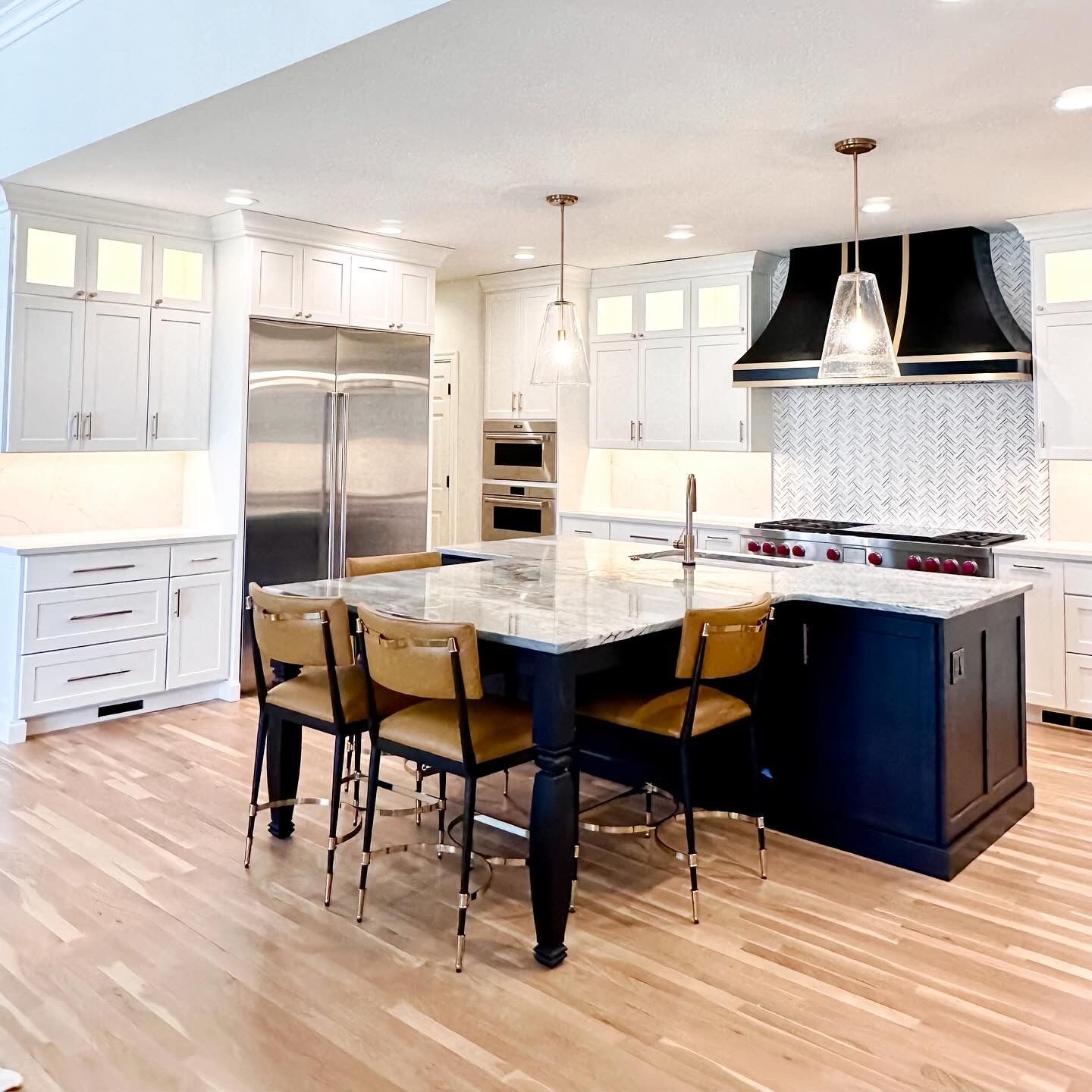 Kitchen with white cabinets, blue island with stools, stainless steel appliances, and wood floor.