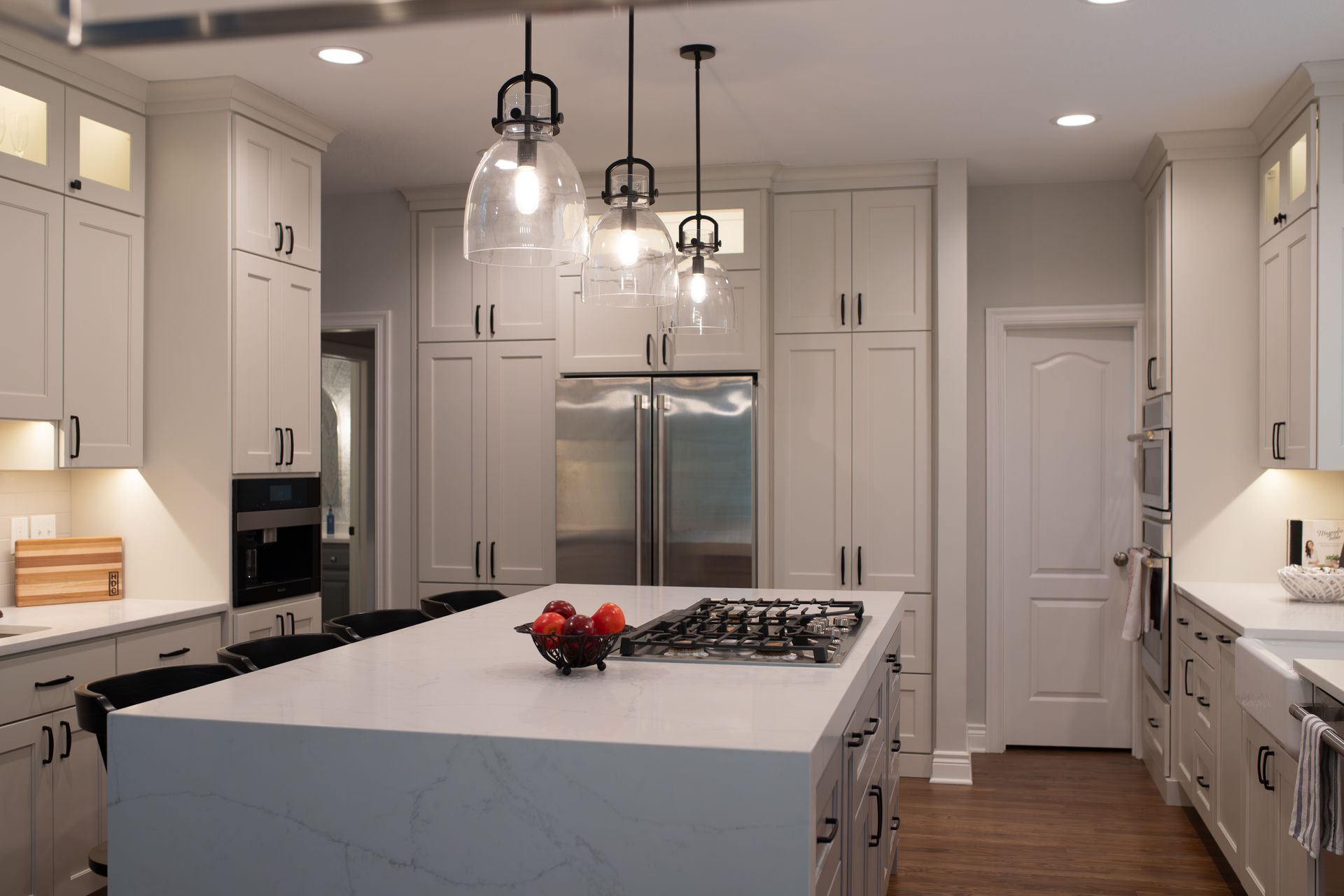 Modern kitchen with white cabinets, island with cooktop, pendant lights, and stainless steel refrigerator.