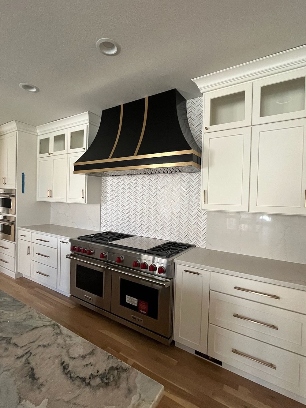 A kitchen with white cabinets, stainless stove, black range hood, and mosaic tile backsplash
