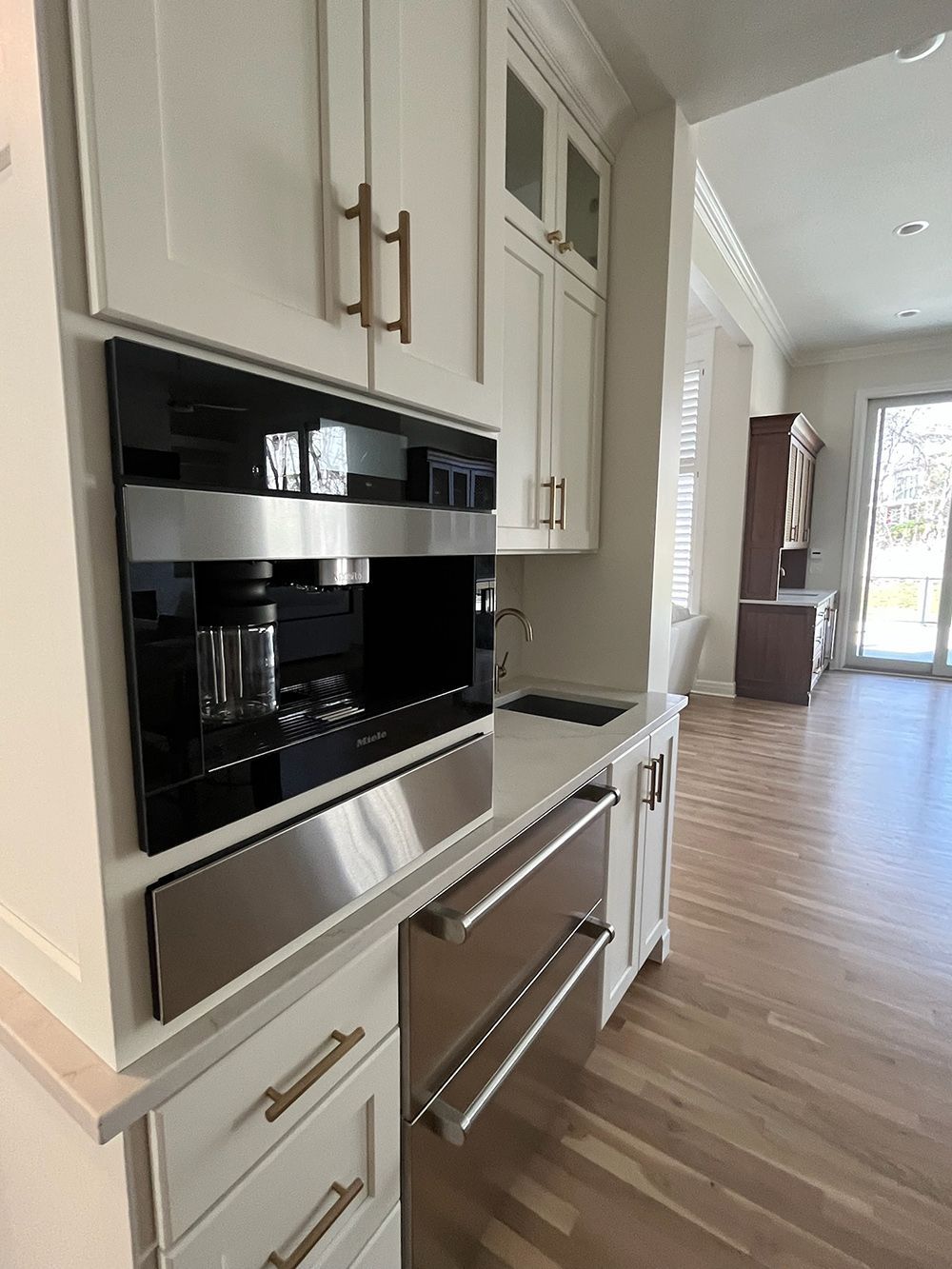 Modern kitchen with white cabinets, black built-in oven, and stainless dishwasher overlooking a bright hallway