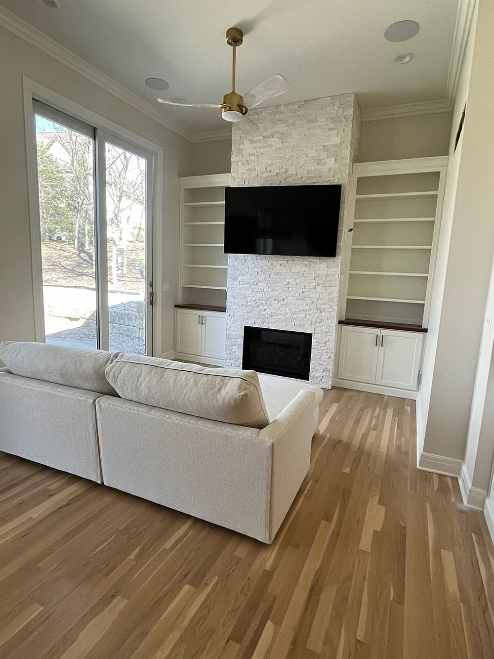 Bright living room with beige sectional, wall-mounted TV, fireplace, built-in shelves, and wood floors