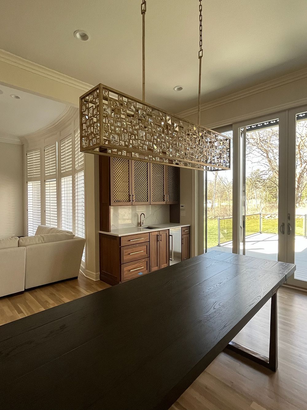 Modern kitchen with a long black table, wood cabinetry, and large windows overlooking a bright yard