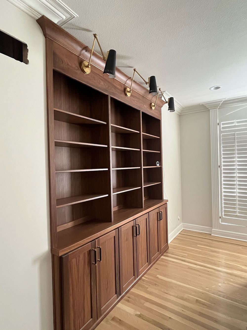 Built-in wooden bookshelf and cabinet in a bright room with hardwood floors and window blinds