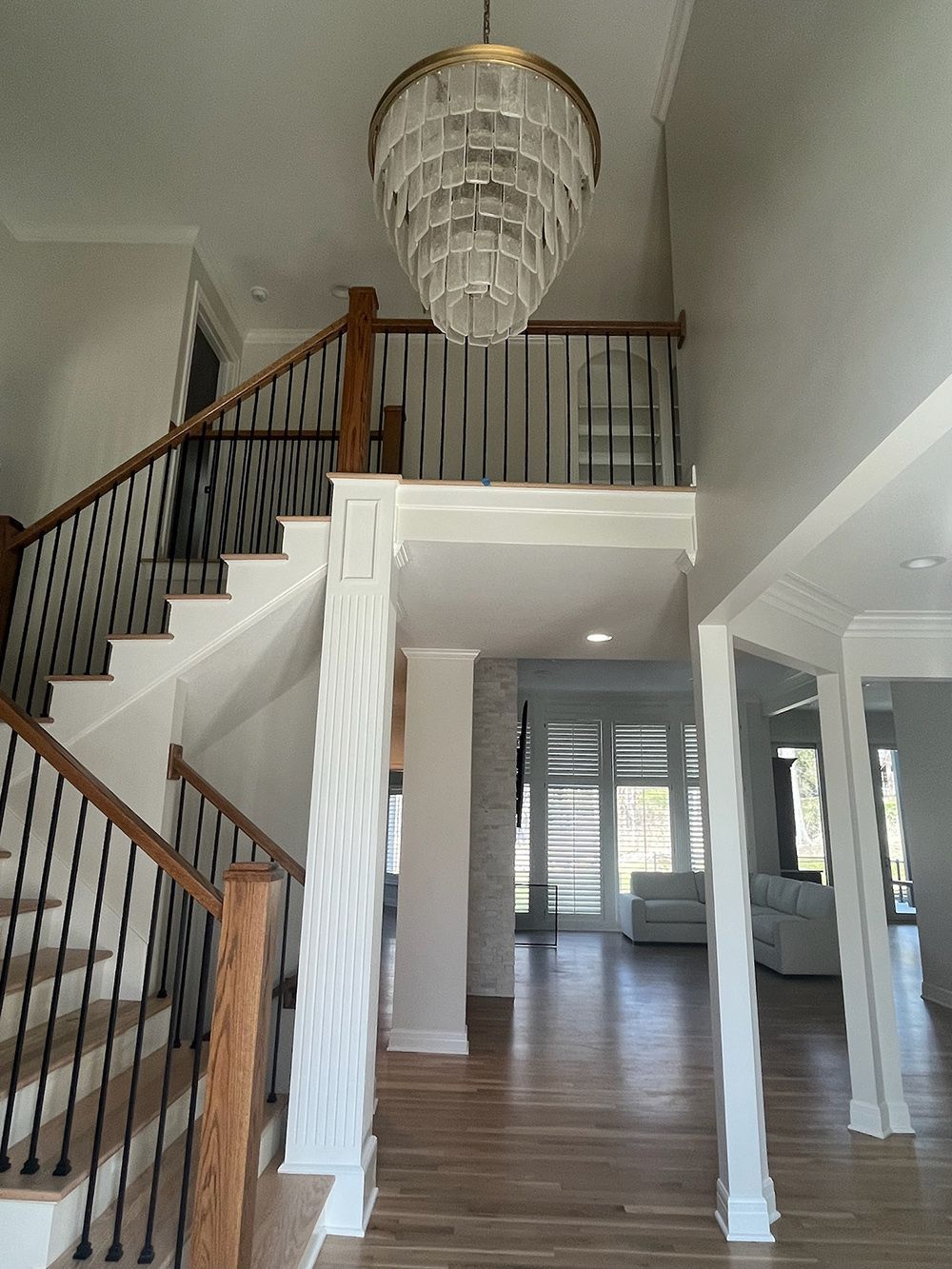 Bright foyer with staircase, chandelier, wood floors, and white columns opening to a hallway.