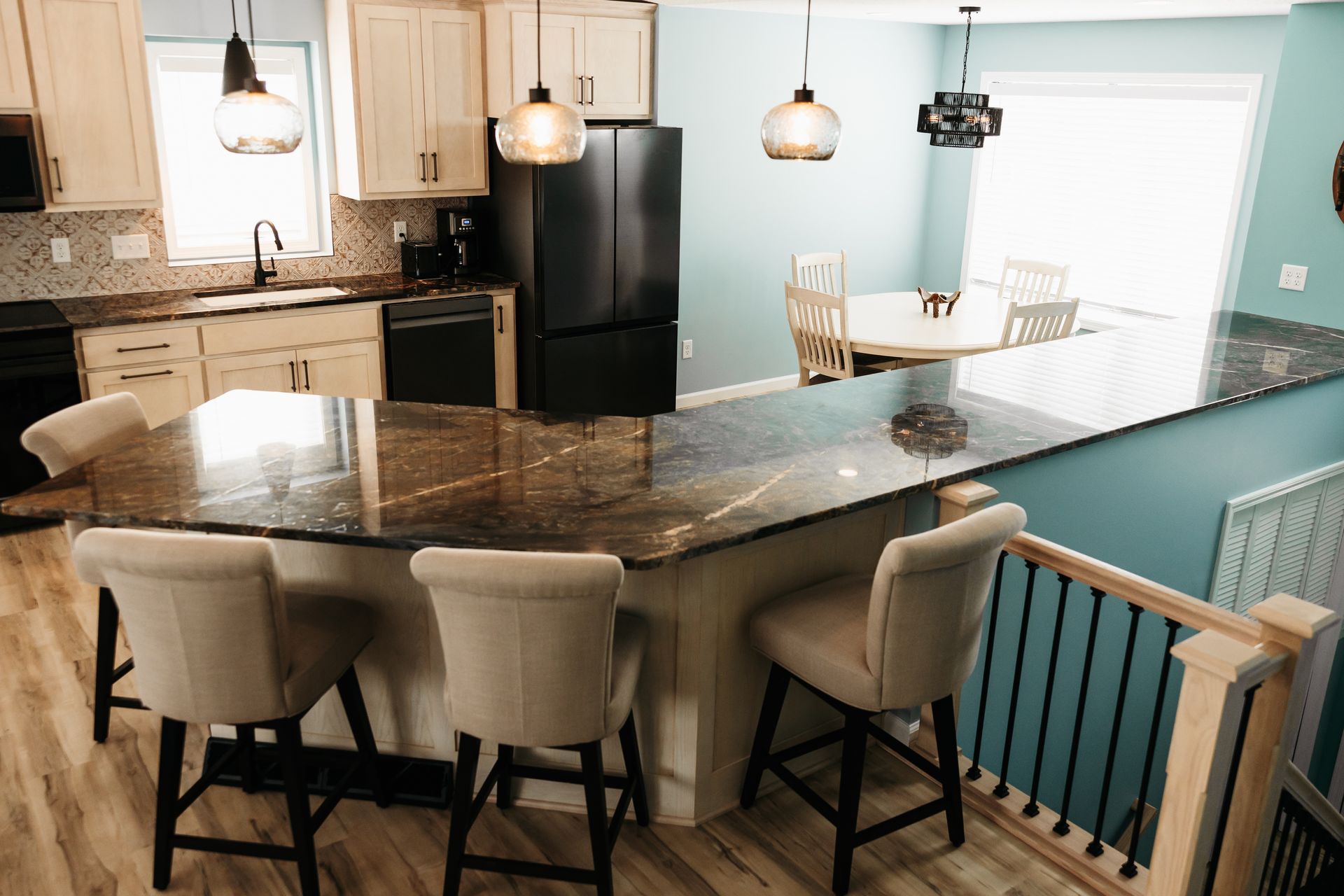 A kitchen with a breakfast bar, dining table, and black appliances. Neutral tones with blue wall and light-colored bar stools.