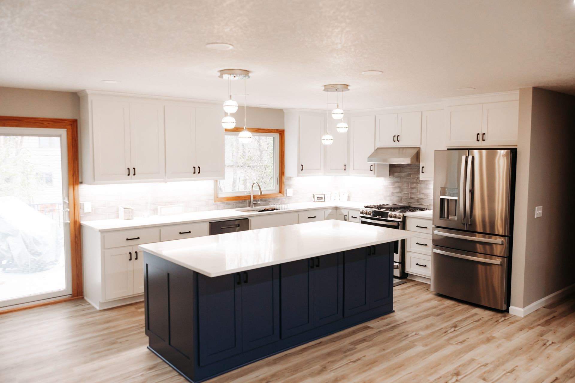 Modern kitchen with white cabinets, navy blue island, stainless steel appliances, and light wood floors.