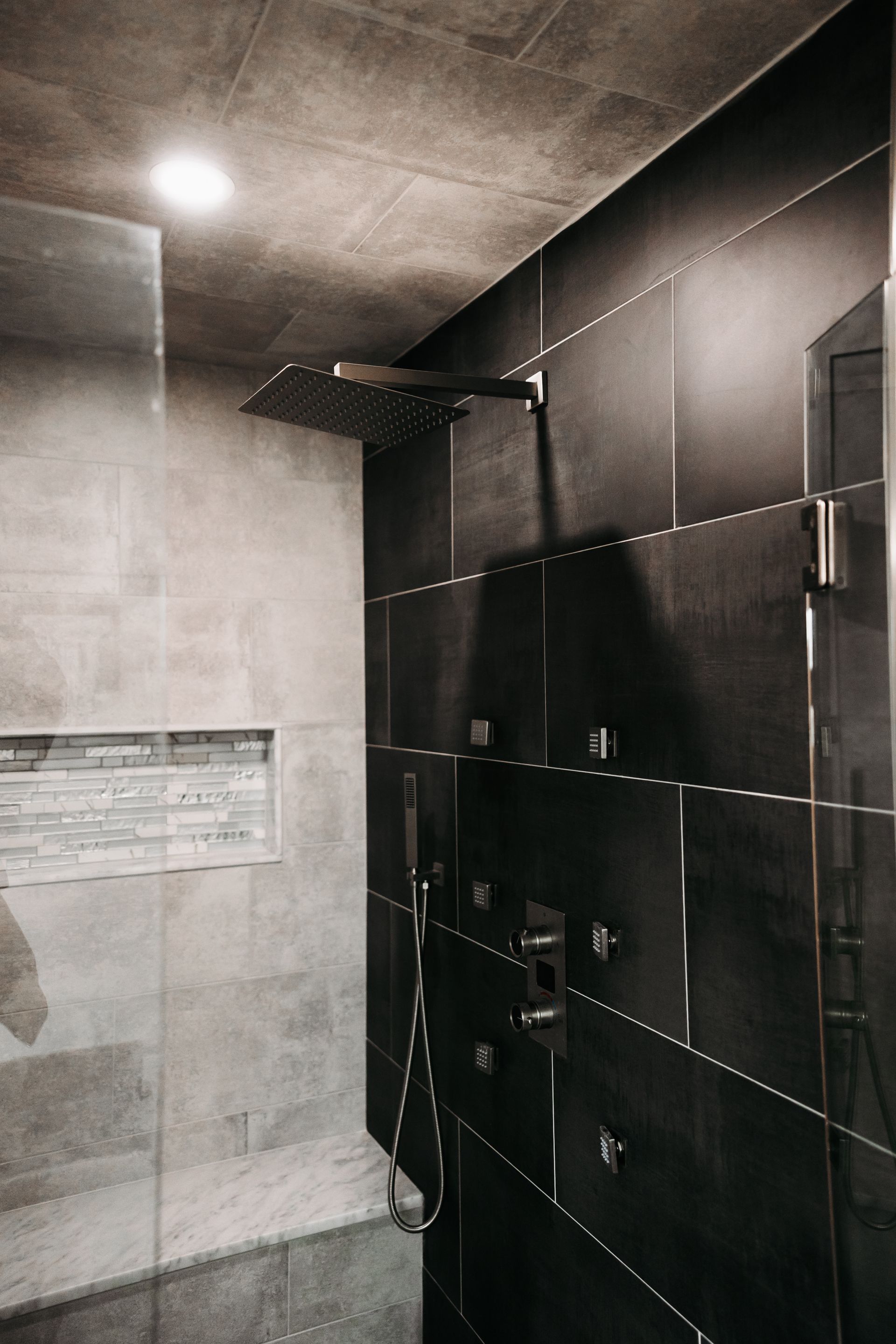 Modern shower with dark and light gray tile, large square showerhead, and in-wall shelving.