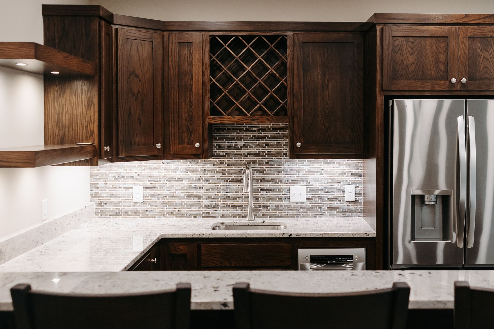 A built-in home bar with dark wood cabinets, granite countertops, a wine rack, and a stainless steel refrigerator.
