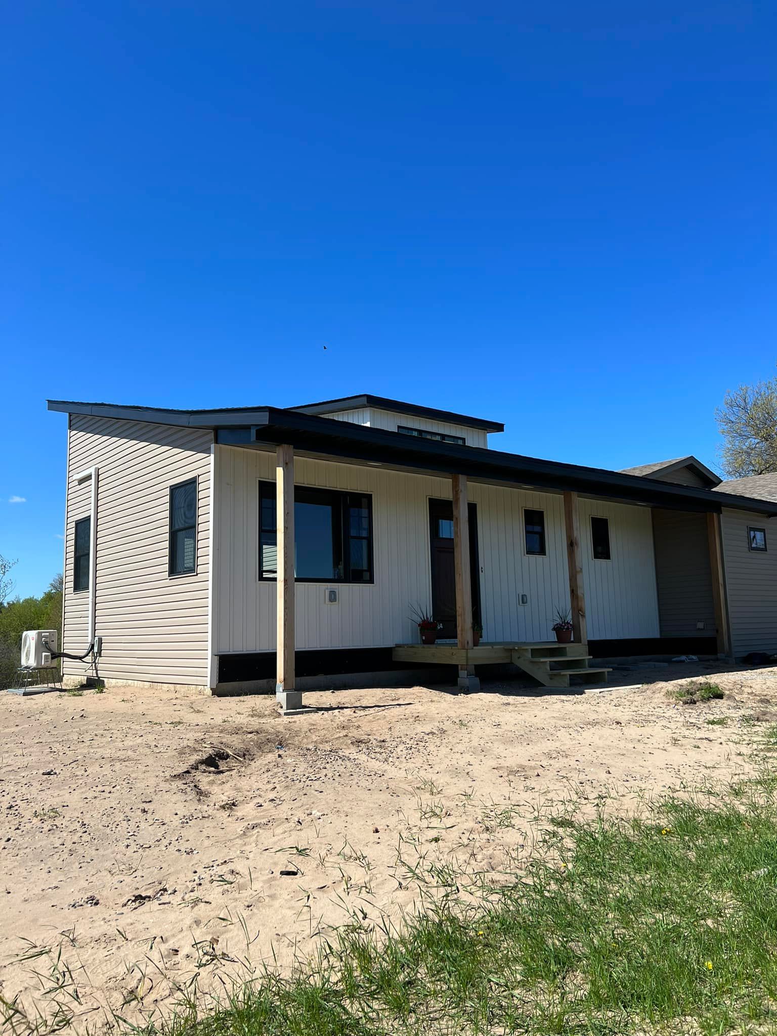 A small white house with a porch in the middle of a dirt field.