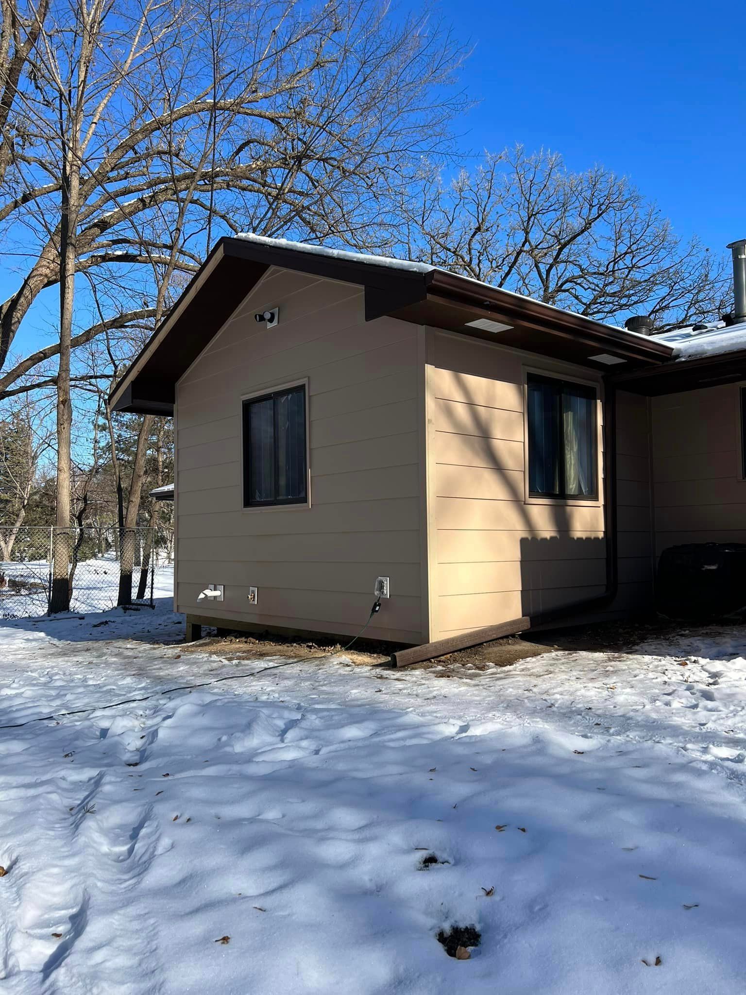 A small house is sitting in the middle of a snowy field.